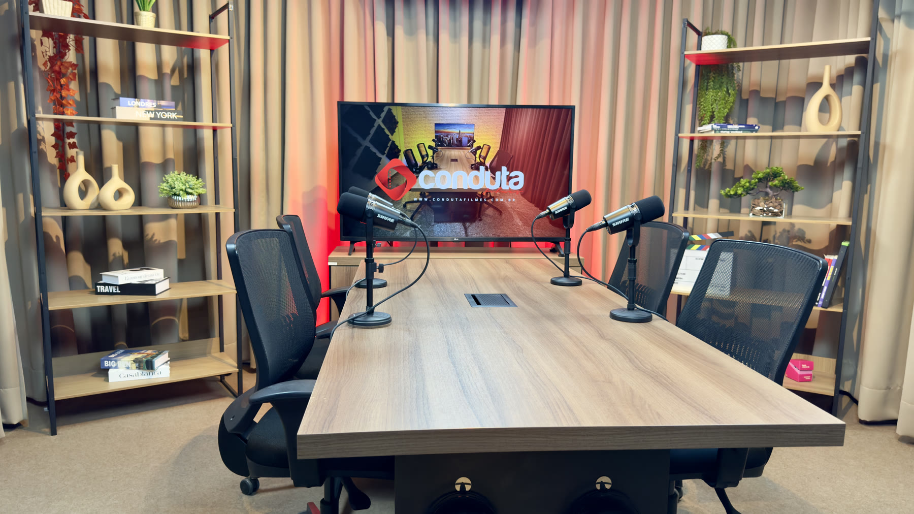 Mesa do estúdio de podcast com microfones e TV